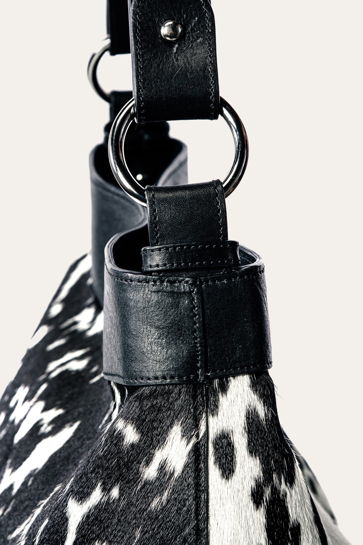Close-up of a black leather strap with a metal ring on a cowhide bag.