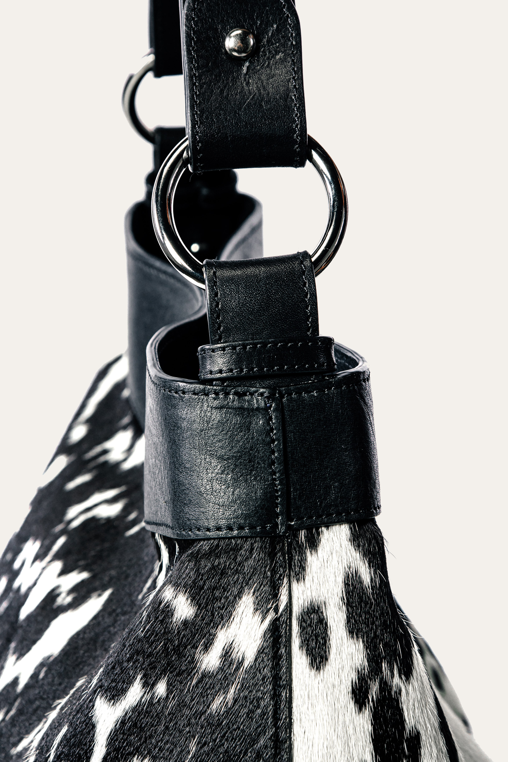 Close-up of a black leather strap with a metal ring on a cowhide bag.